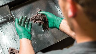 Mann mit Arbeitshandschuhen putzt eine stark verschmutzte Oberfläche